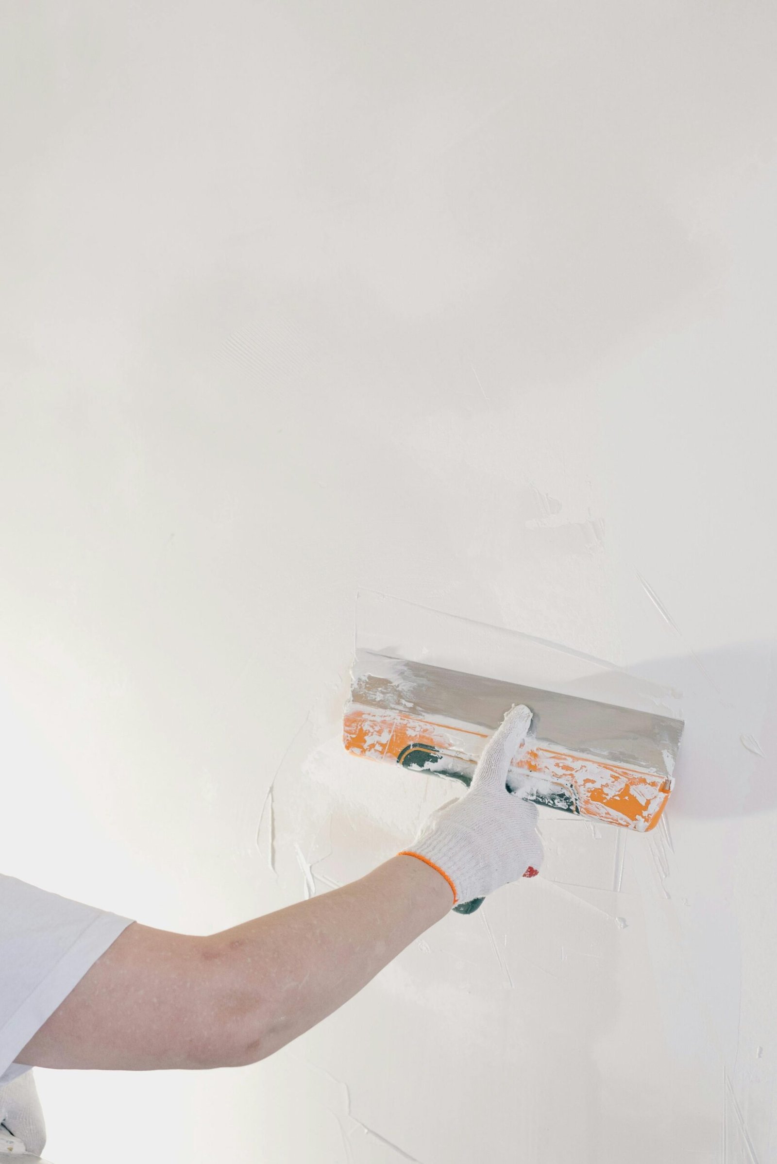 Close-up of a gloved hand plastering a wall with a spatula in a home renovation setting.